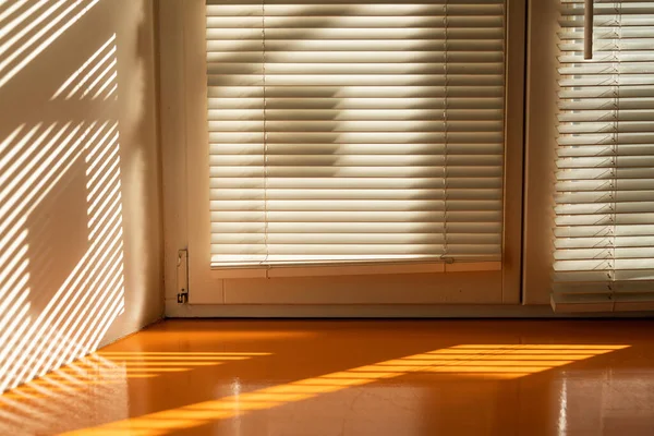 Oblique lines of morning light through white wooden blinds on a wooden orange window sill and white wall, abstract geometric background, play of light and shadow