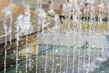 Seçici odak noktası, şehrin fıskiyesinin su fışkırtmaları güneşli bir günde arka planda, sıcak yaz havası şehirde.