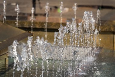 Seçici odak noktası, şehrin fıskiyesinin su fışkırtmaları güneşli bir günde arka planda, sıcak yaz havası şehirde.