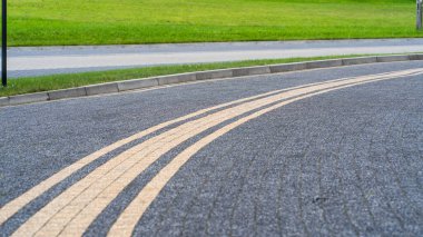 Concrete or cobblestone gray square paving slabs go to the right corner of the frame, green lawn, stone pavement, road geometry, road markings for cyclists