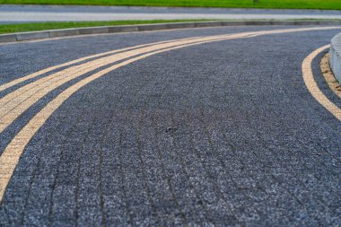 Concrete or cobblestone gray square paving slabs go to the right corner of the frame, green lawn, stone pavement, road geometry, road markings for cyclists