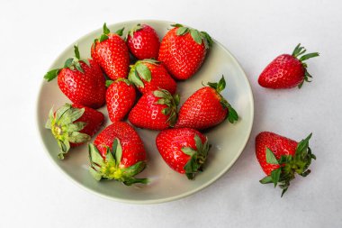 Red ripe strawberries in a light green bowl, light background, top view, healthy food, natural vitamins.Copy space