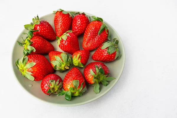 Red ripe strawberries in a light green bowl, light background, top view, healthy food, natural vitamins.Copy space