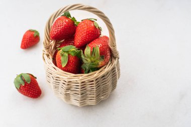 Red ripe strawberries in a white wicker basket on a white marble table surface, light background, side view, healthy food, natural vitamins