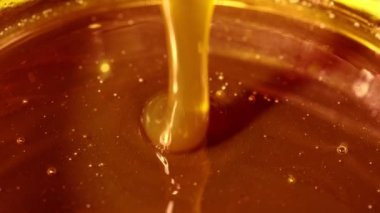 A flow of flower honey flows into a glass jar with natural honey, reflections on the surface of honey, sweet organic product