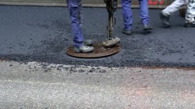 Replacing old asphalt when repairing the road surface. A road worker in uniform using a special tool lays a manhole cover on a well on a road with new asphalt. Repair and reconstruction of pavement