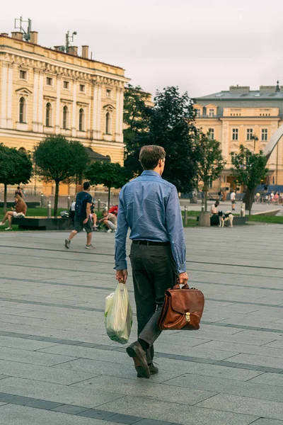 A young man with a business briefcase walks down a city street from a shopping center in the evening, shopping in a recycled plastic bag. Selective focus, copy space