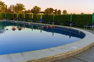 The blue sky is reflected on the surface of the outdoor pool, the summer beautiful pool in the hotel, comfortable summer vacation in Italy, the play of reflections on the surface of the water