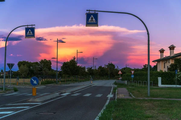 Sunset over the road and crosswalk, street lighting electric poles along the road on the outskirts of the city in Italy, crosswalk signs sky at sunset, sunset sky background image