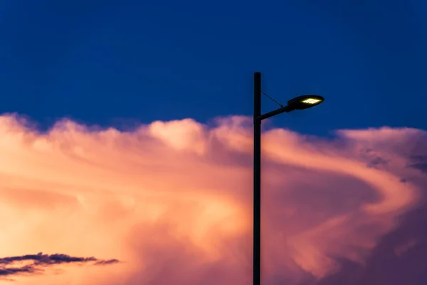 LED street lighting lamp on electric pole illuminates the street against white cloud in the sky after sunset, street lighting electric poles in Italy, sky at sunset, sunset sky background image