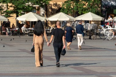 Güneşli bir yaz gününde eski kasabada el ele tutuşan bir çift at arabalarına ve arka planda bir yaz restoranına doğru yürüyor. Birkaç turist, yetişkin bir çift.