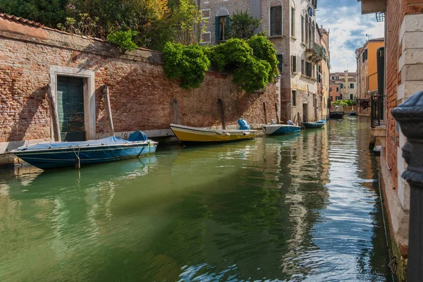 Boats near a vintage brick wall on the water surface of a narrow canal street in Venice, reflections of old houses with windows on a Venetian street, Venice canal on a sunny day