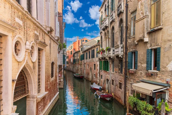 Boats near a vintage brick wall on the water surface of a narrow canal street in Venice, reflections of old houses with windows on a Venetian street, Venice canal on a sunny day