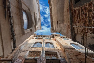 Mavi gökyüzünün altında yüksek pencereli eski duvarlar güneşli bir sabahta Venedik 'te beyaz bulutlar Venedik pencerelerinde ahşap panjurlar, eski binalar Venedik' te eski duvarların dokusu, aşağıdan manzara.