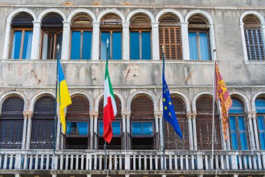 Ukrayna bayrağı, Avrupa Birliği bayrağı, İtalya ve Venedik bayrağı Venedik şehrinde açık havada eski bir tarihi binanın duvarında rüzgarda dalgalanıyor..