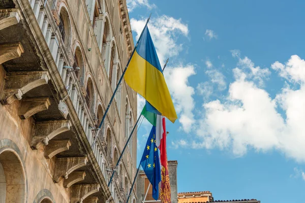 Ukrayna bayrağı, Avrupa Birliği bayrağı, İtalya ve Venedik bayrağı Venedik şehrindeki mavi gökyüzüne karşı eski bir tarihi binanın duvarında rüzgarda dalgalanıyor.