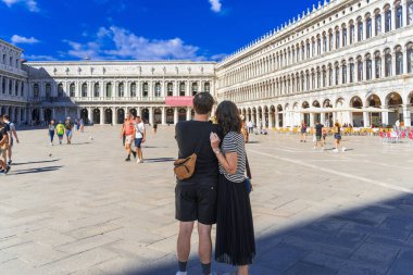 Güneşli bir sabahta Venedik 'te St. Mark' s Bazilikası ve St. Mark 's Bell Tower (Campanile di San Marco) ile St. Mark Meydanı' na bakan iki genç turist İtalya 'ya seyahat ediyor.