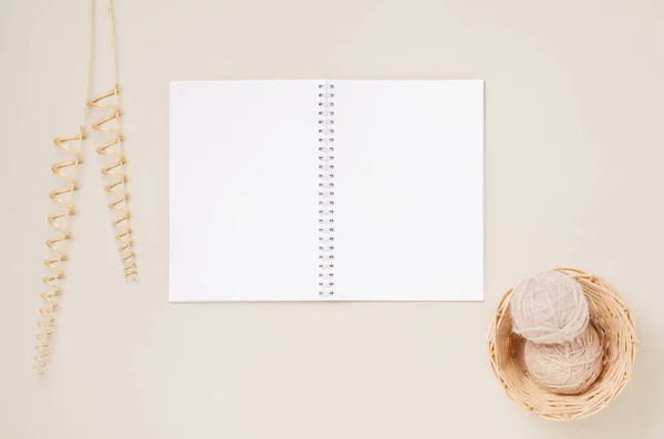 Un quaderno bianco, fili in un cesto di vimini e un ramo decorativo da una vite secca. Sfondo beige. Copia spazio. — Foto Stock