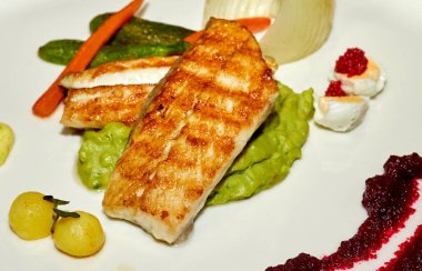 Sebzeli ızgara balık filetosu ve beyaz tabakta yeşil sos. Restoranda balık yemeği.