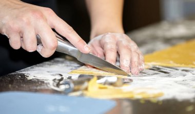 Mutfaktaki aşçı erişte için hamuru ince şeritler halinde bıçakla keser. Erkek elleri yakın.