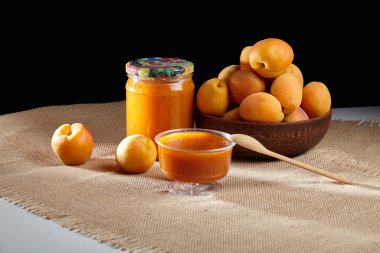 Cam kavanozlarda ev yapımı kayısı reçeli. Portakal reçeli kavanozlarının etrafındaki masada taze kayısılar.