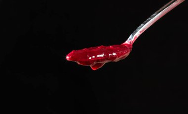 Red sauce for meat in a metal spoon on a black background close-up. Tkemali