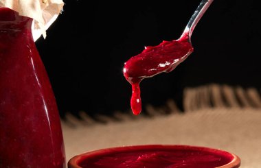 Red sauce for meat in a glass bottle with a metal spoon on a black background close-up. Tkemali