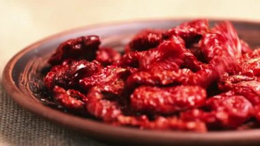 Dried tomatoes fall into a clay bowl. Smooth horizontal camera movement. Close-up shot with blurry background