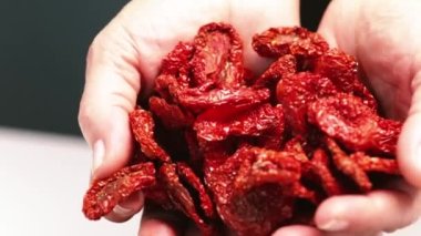 Dried tomatoes in female hands fall into a clay bowl. Close-up shot with blurry background