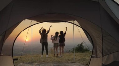 Bir grup genç Asyalı arkadaş gün batımında bir yaz kampı tatili sırasında çadırın önünde durup fotoğraf çekiyorlar ve dinleniyorlar. Özgürlük, rahatlık, seyahat, macera konsepti