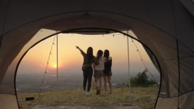 Bir grup genç Asyalı arkadaş gün batımında bir yaz kampı tatili sırasında çadırın önünde durup fotoğraf çekiyorlar ve dinleniyorlar. Özgürlük, rahatlık, seyahat, macera konsepti