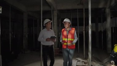 Acele mesai saatlerinde, mühendisler ve mimarlar arka planda çeliği öğüten inşaat işçilerinin olduğu bir inşaat sahasında danışmanlık yapıyorlar..