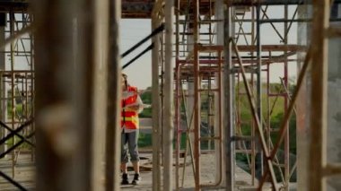 Genç Asyalı kadın mühendis ve ustabaşı inşaatın plana uygun çalışıp çalışmadığını kontrol etmek için inşaat alanında yürüyorlar..