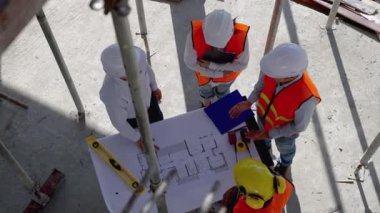 Dış inşaat sahalarında, Asyalı mühendisler ve mimarlar inşaat için danışmanlık ve planlama yaparken, form ve çizelgeye göre tamamlanmak üzere binanın el ele tutuşuyorlar..