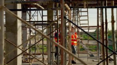 Genç Asyalı kadın mühendis ve ustabaşı inşaatın plana uygun çalışıp çalışmadığını kontrol etmek için inşaat alanında yürüyorlar..