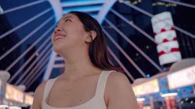 Geceleri, genç Asyalı kadın tabletle mutlu bir şekilde oynuyor. Umutlar ve hayallerle ileriye bakıyor. Günümüzün teknolojisi, şehir toplumunun ortasında, arka planda binalar olan bir yerde..