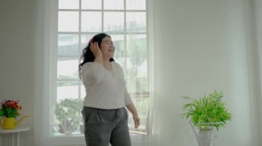 Şişman kadın ya da kilolu kadın evde müzik dinleyerek rahatlıyor, yavaşça sallanıyor. Müzikte mutluyuz. Sosyal uzaklık konsepti, evde rahatlama..
