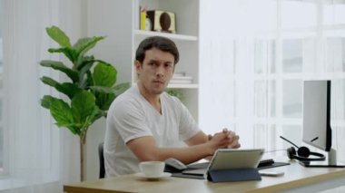 Günlük giysiler içindeki genç adam, sosyal medyada insanlarla uğraşan bir bilgisayar ve tabletle evde çalışmaktan stresli. Sosyal uzaklık, her şeyin interneti..