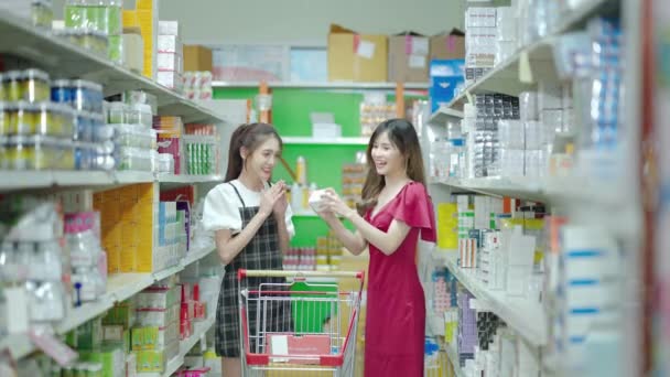 2人の若いアジアの友人がスーパーで楽しみながらショッピングカートを歩いています — ストック動画