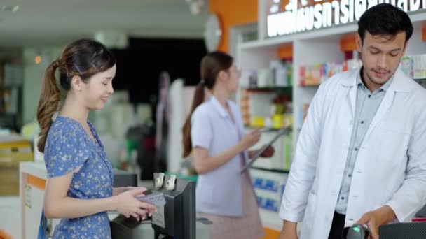 原因アジア系男性薬剤師が処方に従って患者または顧客に薬箱の薬理特性を説明し 顧客にカスタムで電子サービスの支払いを提供する — ストック動画