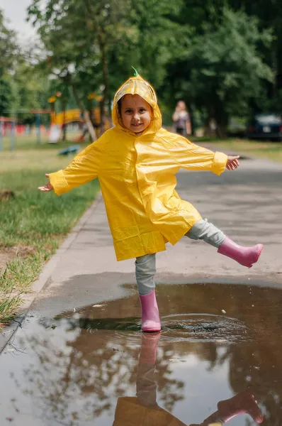 Chica en un vestido amarillo con un paraguas alegre primavera corre a través de los charcos en un día lluvioso —  Fotos de Stock