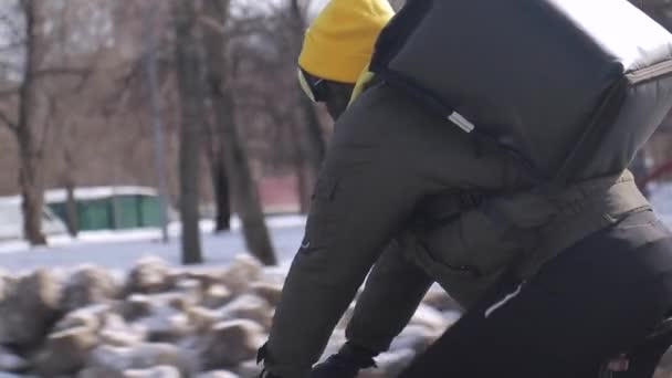 Posłaniec rowerowy z workiem chłodzącym za plecami jeździ rowerem po zimowej drodze — Wideo stockowe