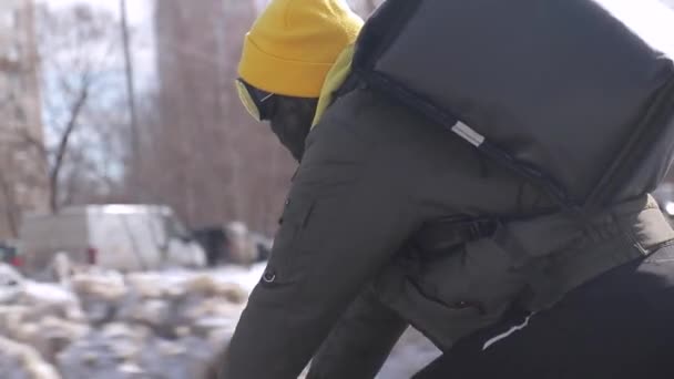 Livreur avec sac refroidisseur derrière son dos monte un vélo sur une route d'hiver — Video