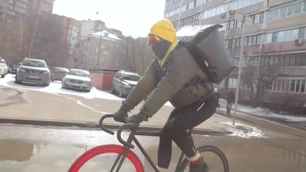 Велокурьер с более прохладной сумкой доставляет заказ на велосипеде. Солнечный зимний день — стоковое видео