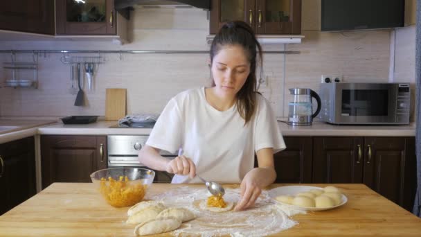 Жінка робить яблучний пиріг на дерев'яному столі з борошном і яблучними пирогами поруч — стокове відео