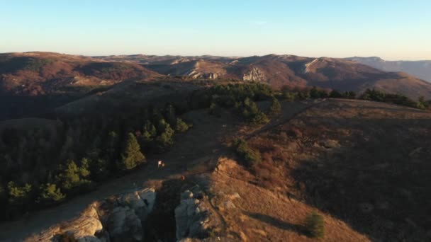 Drone voa sobre terreno montanhoso e floresta com estrada no outono ao amanhecer — Vídeo de Stock