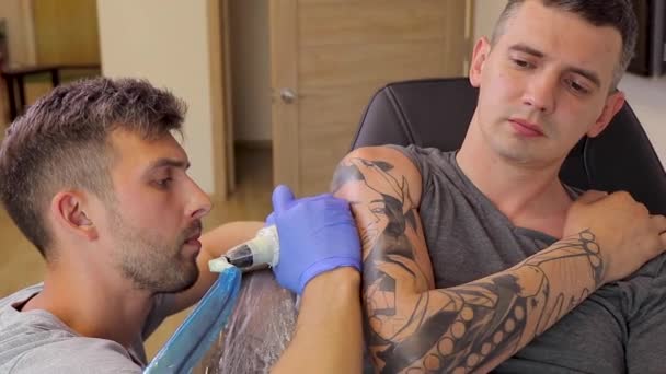 Tattoo artist fills tattoo on the shoulder with tattoo machine in tattoo parlor — стоковое видео