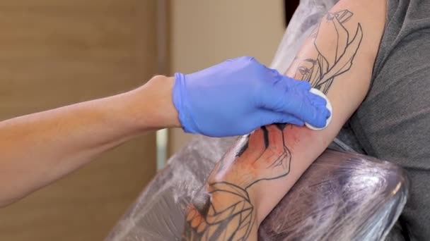 Tattoo artist wipes protruding blood from shoulder after tattooing — Vídeo de Stock