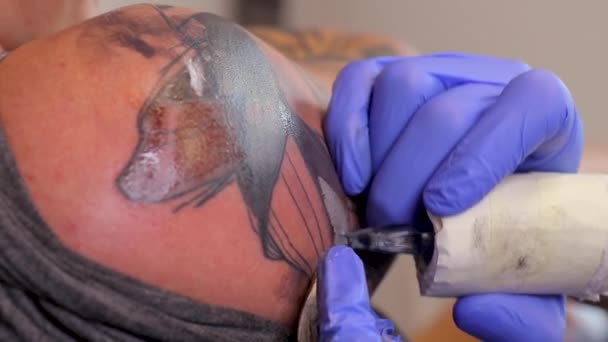 O artista de tatuagem faz uma tatuagem em uma pele de homem com uma máquina de tatuagem. Fechar — Vídeo de Stock