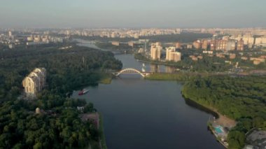 Drone shooting a green area with high-rise buildings, river and bridge in summer